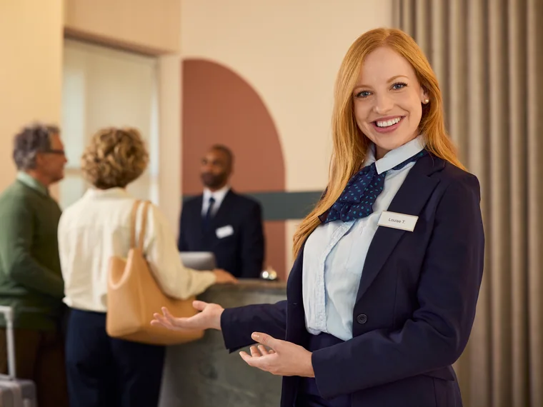 Une réceptionniste qui accueille des clients à l’entrée d’un hôtel