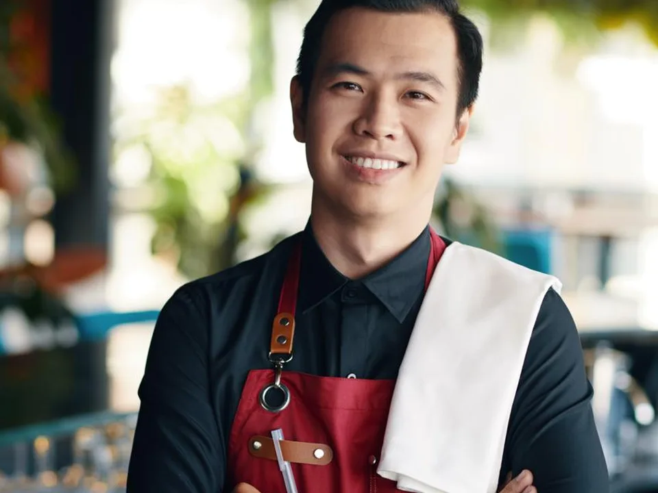 Un serveur souriant derrière le comptoir de son restaurant